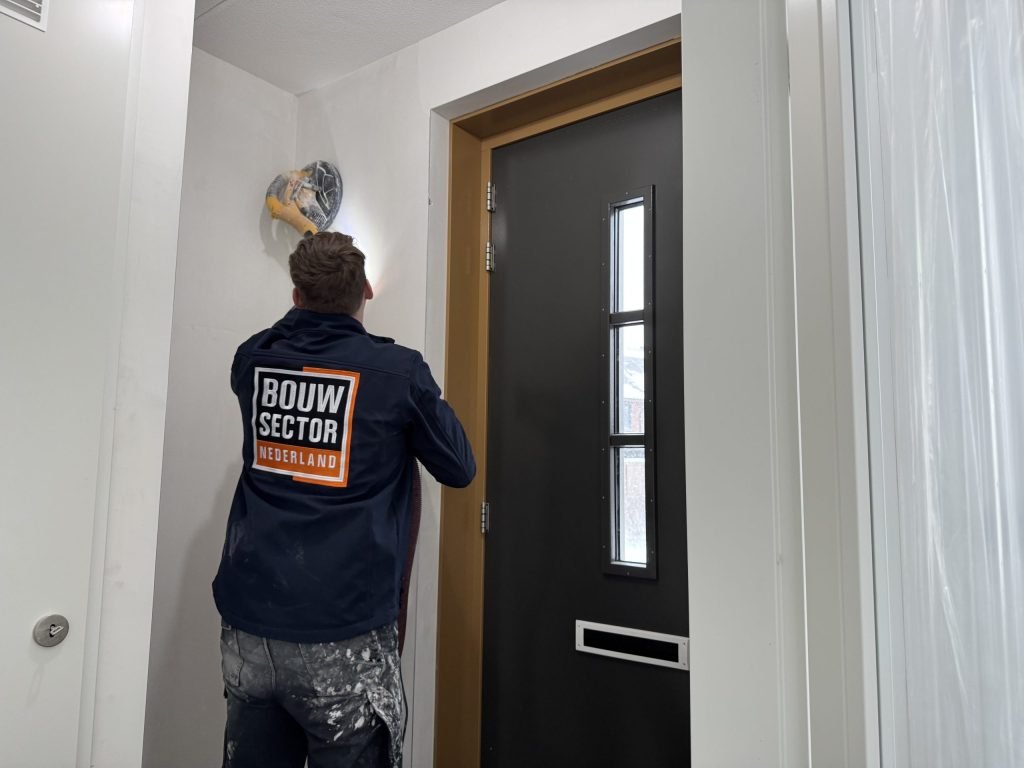 Vakman schuurt de bovenkant van een gestucte wand en de aansluiting met het plafond bij de hal