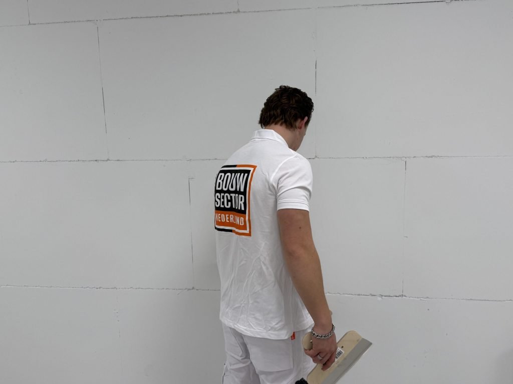 Stukadoor met spaan in de hand bekijkt een kale muur van kalkzandsteen voordat hij begint