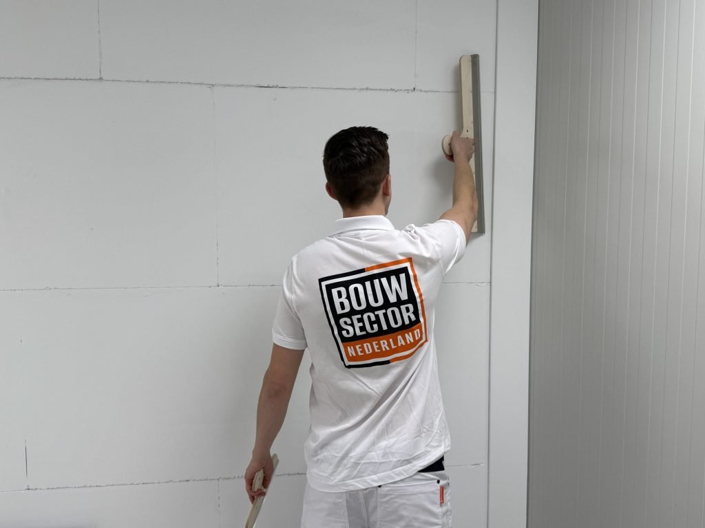 Stukadoor in wit werkshirt houdt een spaan tegen een muur van kalkzandsteen om de laag vlak te zetten