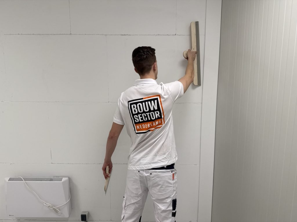 Stukadoor van Bouwsector Nederland werkt met een lange spaan boven zijn hoofd een wand glad