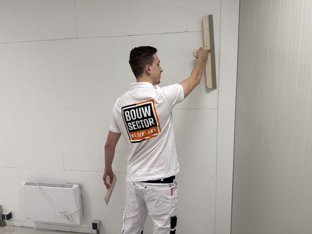 Stukadoor trekt met een brede spaan een wand van kalkzandsteen vlak, naast een elektrische kachel