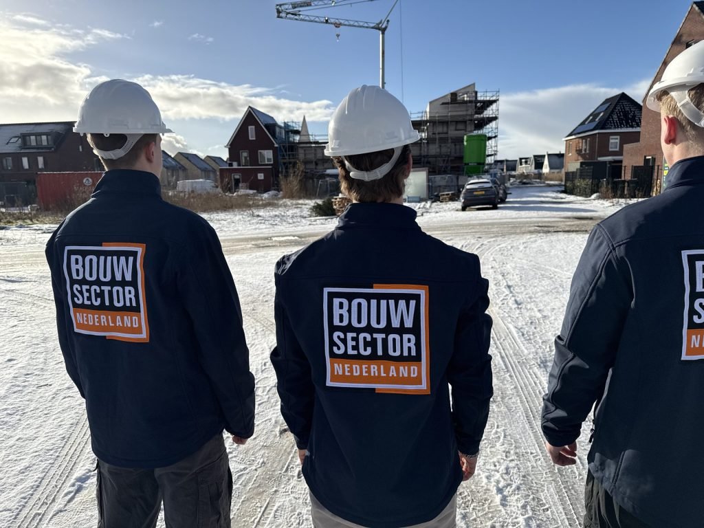 Drie vakmensen van Bouwsector Nederland met helm kijken over een straat met woningen die net gebouwd worden